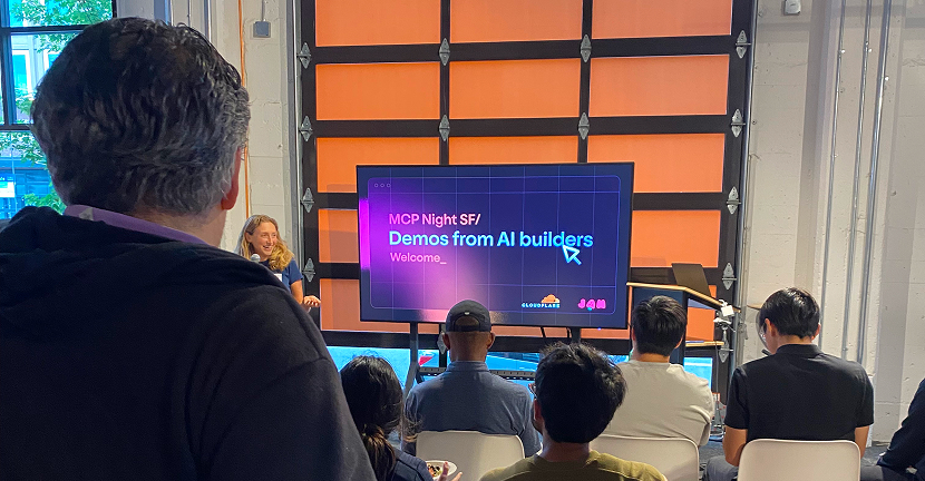 サンフランシスコの会場で行われたAI開発者向けイベント「MCP Night SF」のデモセッション。スクリーンに「Demos from AI builders」と表示され、参加者が発表を見守っている。