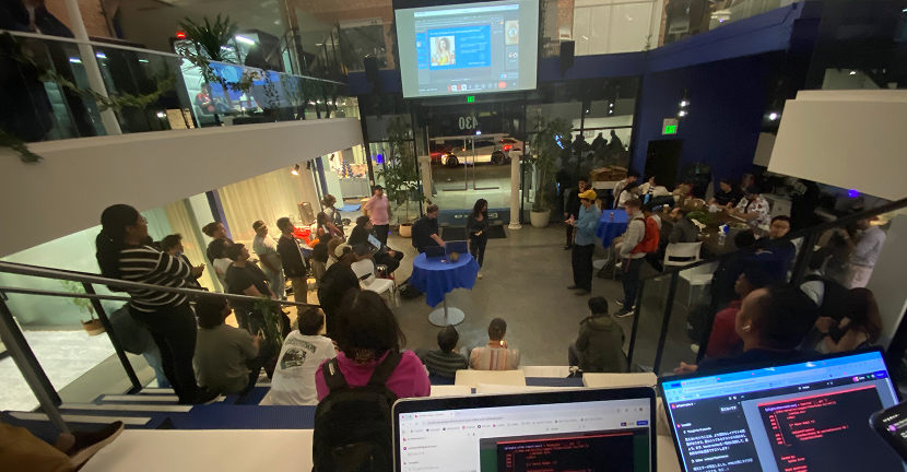 二階建てのスペースで開催されたAI系イベント。下の階では登壇者が話し、上階から多くの参加者が見守っている。ノートPC画面にはコードやスライドが映し出されている。
